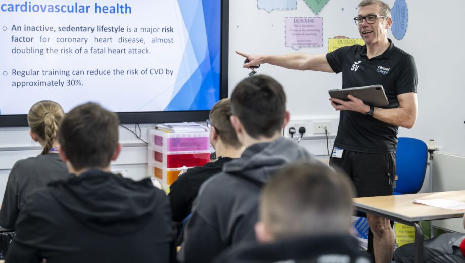 Reacher pointing at whiteboard in front of class of students
